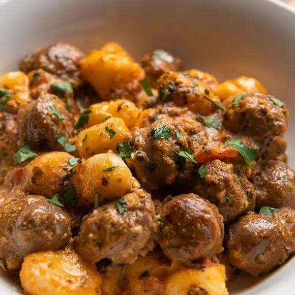 A close up of Italian sausage with gnocchi, topped with green herbs and served in a white bowl.