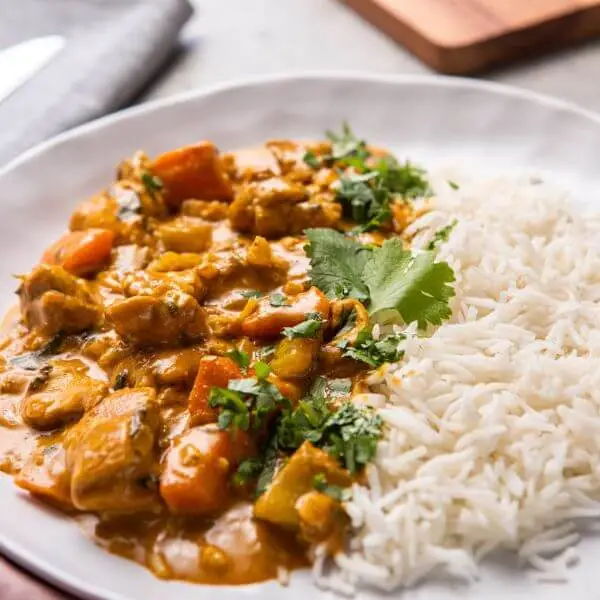 A close-up view of Chicken Masala with Basmati Rice, highlighting the tender chicken pieces coated in creamy, spiced curry and paired with fluffy basmati rice. Freshly chopped parsley is sprinkled on top, adding a pop of color to the hearty dish.