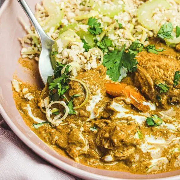 An action shot of Chicken Masala with Cauliflower Rice, showing a fork lifting a piece of tender, spiced chicken from the plate. The dish, garnished with fresh parsley, showcases the vibrant gravy and wholesome cauliflower rice, perfect for a nutritious and flavorful meal.