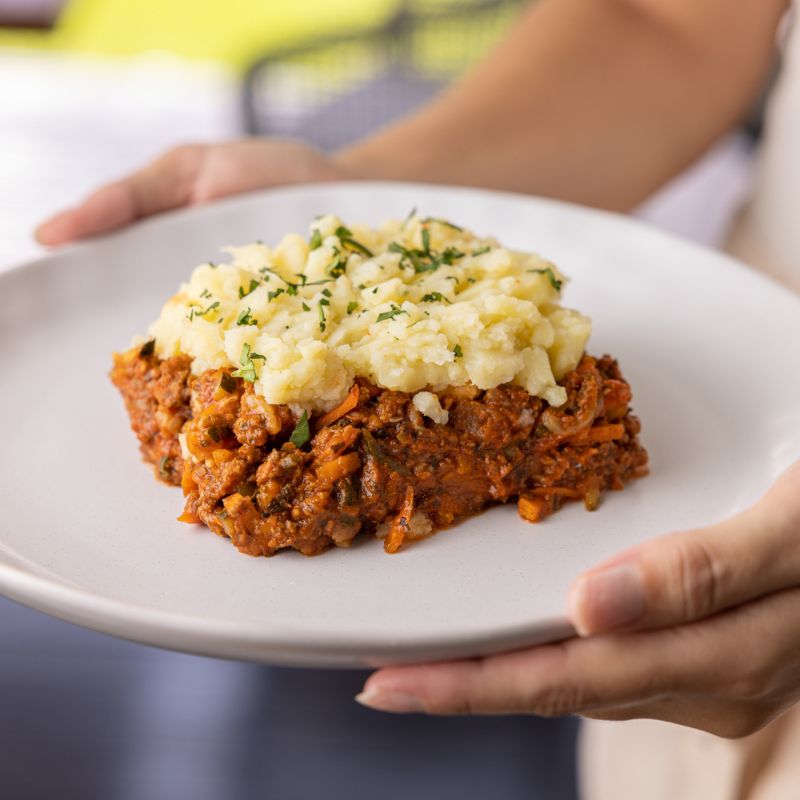 Close-up shot of the Cottage Pie, highlighting the golden-brown potato topping, the savory beef mince, and vegetable filling. The garnished parsley adds a touch of color and freshness to the rich textures of the dish.