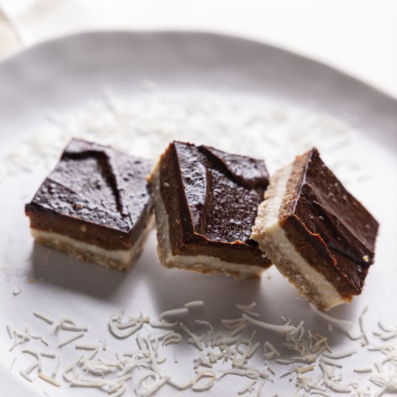 A close up photograph of three salted caramel slices, leaning against each other in a row, served on a white plate with dessicated coconut.