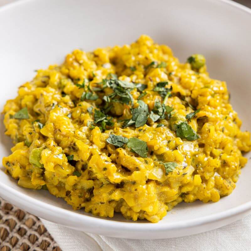 A close-up shot of Pumpkin Risotto, highlighting its creamy, smooth texture and vibrant golden hue. Garnished with chopped spring onion, the risotto looks rich and velvety.