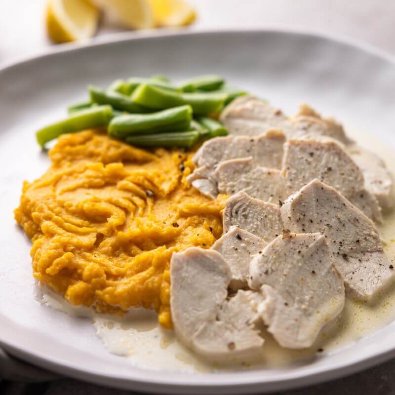 A close-up of Lemon Pepper Chicken, showing the tender chicken breast coated in a creamy lemon pepper sauce, served with vibrant green beans and smooth sweet potato mash. The rich texture of the sauce and the seasoning on the chicken are in sharp detail.