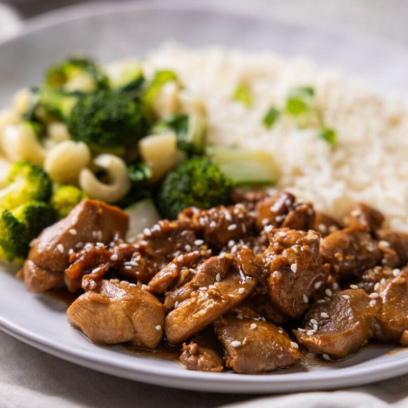 Close-up of Teriyaki Chicken, highlighting the glistening teriyaki sauce, sesame seed garnish, and vibrant steamed broccoli and bok choy.