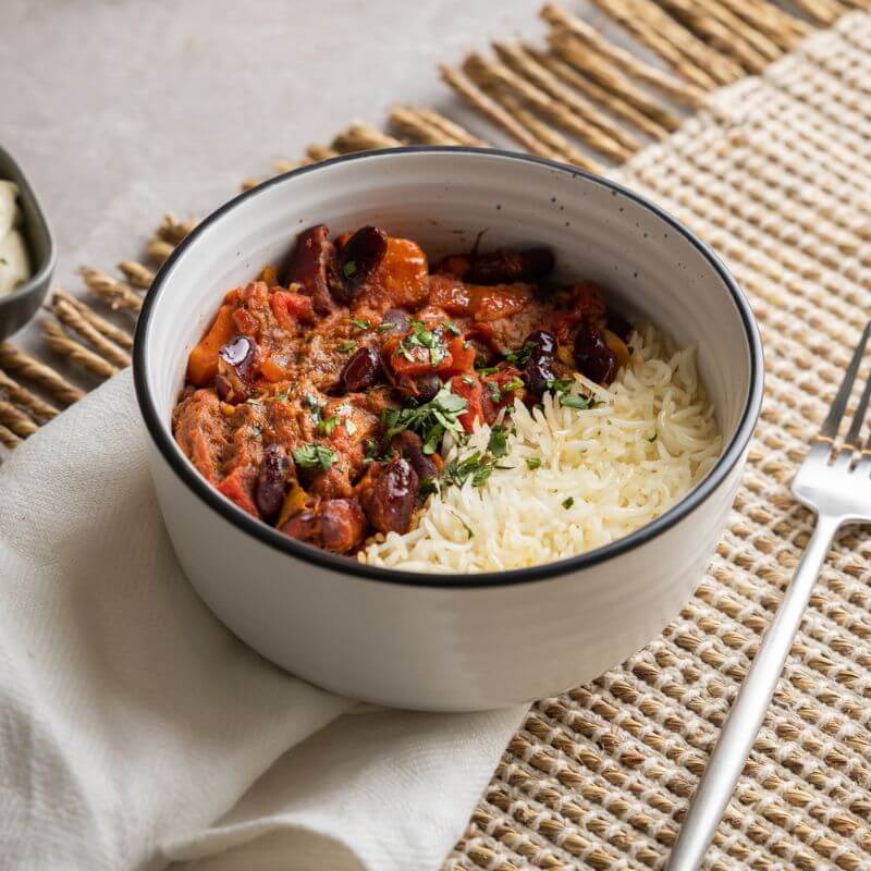 Side shot of Texas Brisket Chilli, with the same elements as in previous photos, highlighting the meal in its rustic setting with parsley garnish on top.