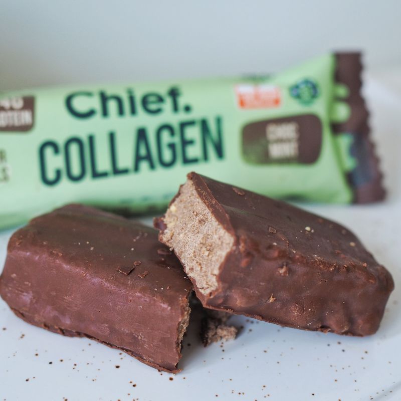 A close up side angle photograph of a cut in half chocolate mint collagen protein bar with the packaging in the background.