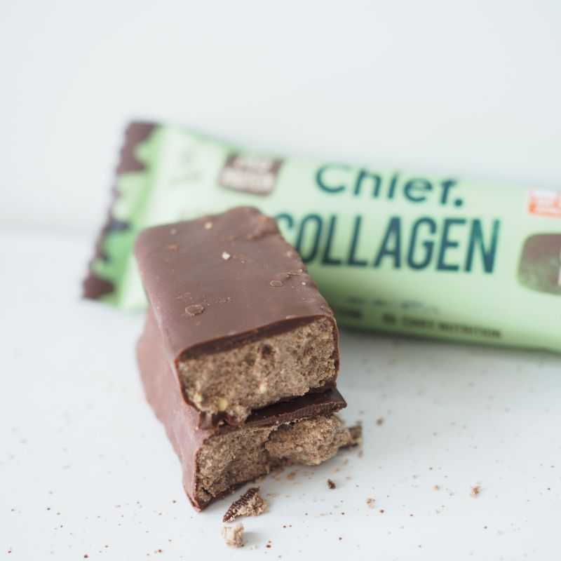 A side angle photograph from the top of a cut in half chocolate mint protein bar where one half is stacked on top of the other. The background is very white, and the packaging lays behind the bar.