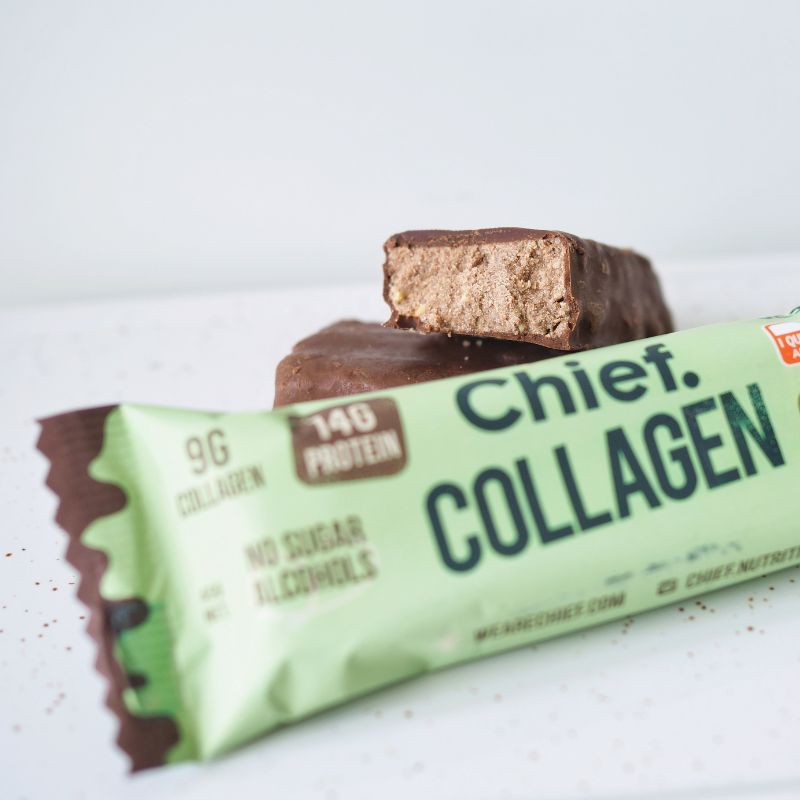 A side angle close up photograph featuring a green choc mint protein bar in the foreground with the bar itself cut in half placed behind. This is all set on a white marble tray.