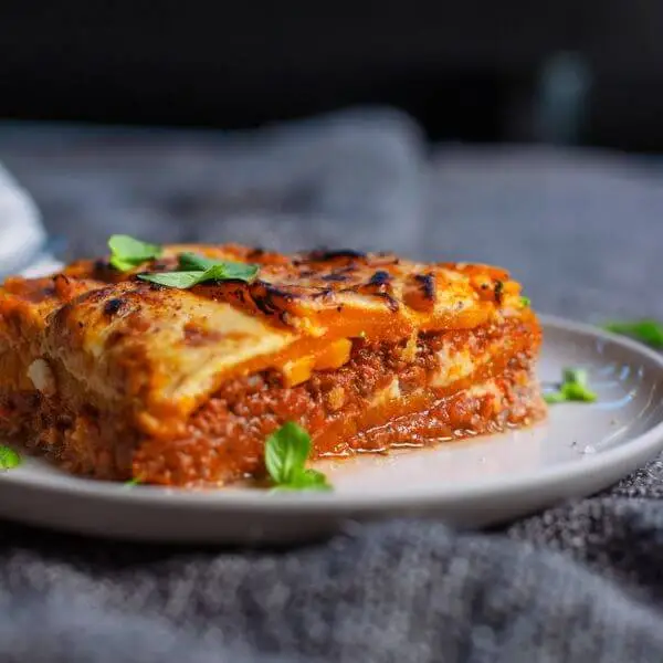 Side shot of the Pumpkin Lasagna, focusing on its depth and layers, showing the rich bolognese, creamy butternut pumpkin, and homemade béchamel sauce. This shot highlights the hearty nature of the meal.