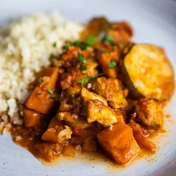 Close-up shot of the Butter Chicken and Cauliflower Rice, highlighting the creamy texture of the curry and the light, fluffy cauliflower rice. The focus is on the vibrant colors and detail of the ingredients.